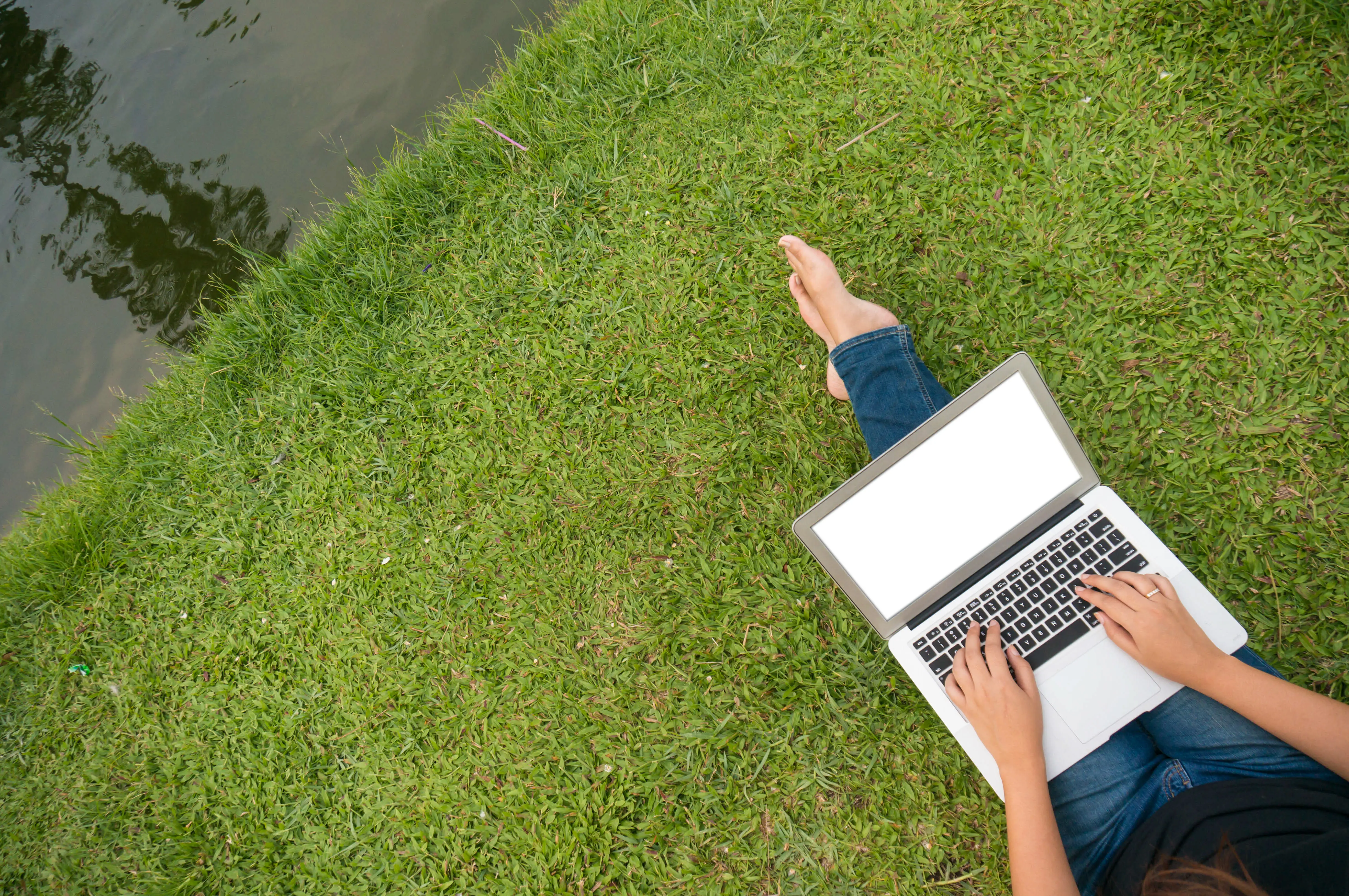 Woman sitting on green grass in a park with a laptop, a student studying outdoors; copy space for text.